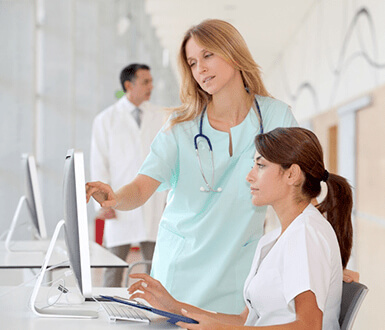 Nurse working with employee in front of computer
