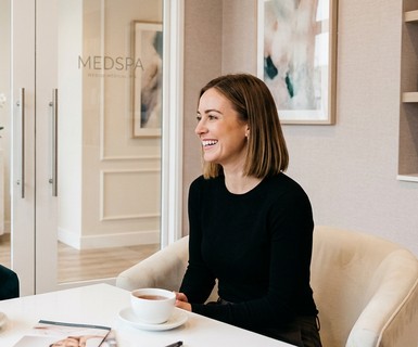 Two medspa clients talking in a bright waiting area, referral word-of-mouth energy, med spa loyalty program driving new client leads